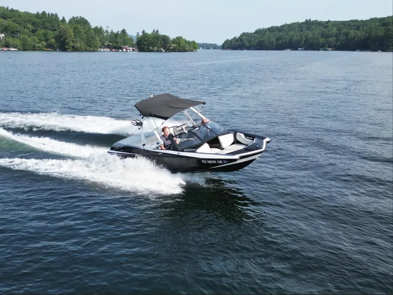 Slide: The Image of 2013 Axis A20 boat cruising on a scenic lake with lush green shoreline. - 18