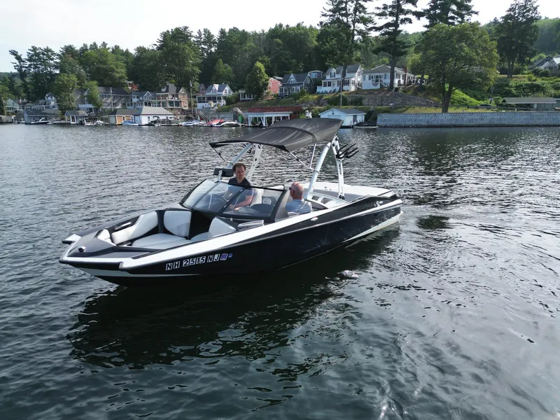 Slide: The Image of 2013 Axis A20 boat on a scenic lake with houses and trees in the background. - 20