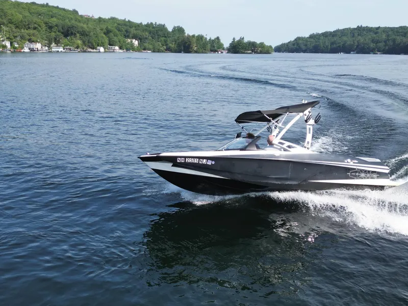 Slide: The Image of 2013 Axis A20 boat cruising on a scenic lake with lush green shoreline. - 22