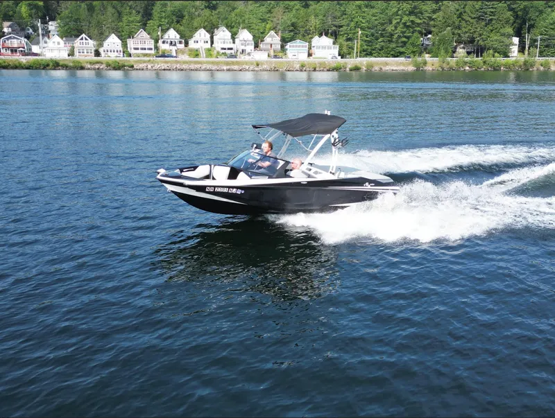 Slide: The Image of 2013 Axis A20 boat cruising on a lake with houses in the background. - 23