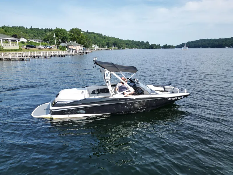 Slide: The Image of 2013 Axis A20 boat cruising on a scenic lake with lush green shoreline. - 6