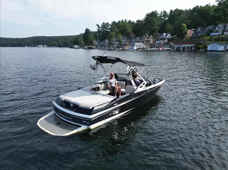 Slide: The Image of 2013 Axis A20 boat cruising on a scenic lake with houses in the background. - 7