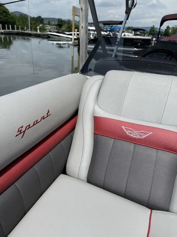 Slide: The Image of 2024 Bennington 24 LXSSB boat interior with red and gray seating at a marina. - 8