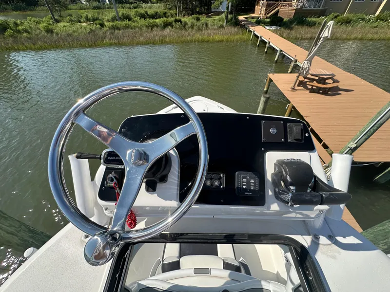 Slide: The Image of 2021 Tidewater 2700 Carolina Bay boat helm with steering wheel and controls by a dock. - 9