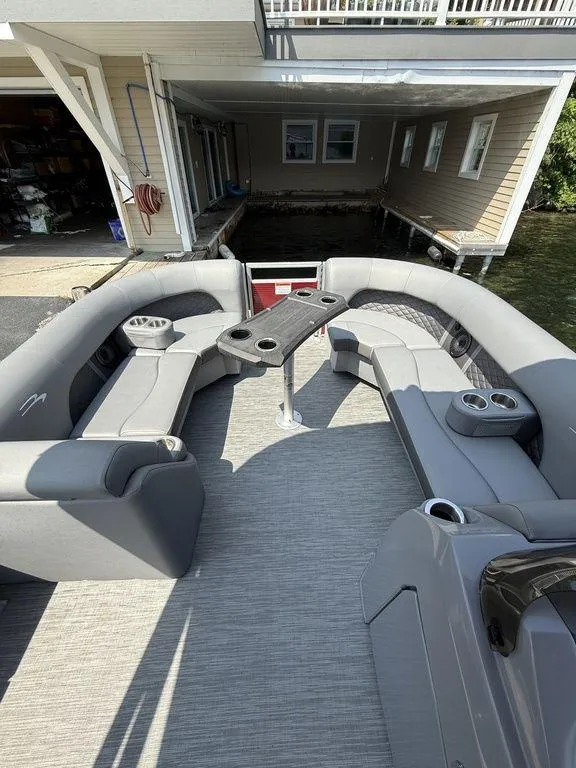 Slide: The Image of 2022 Bennington 23 LSBA pontoon boat with spacious seating and table, docked by a boathouse. - 12