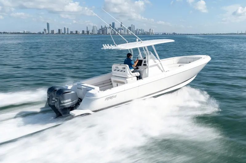Slide: The Image of 2015 Intrepid 327 CC INFUSED boat cruising on water with city skyline in background. - 2
