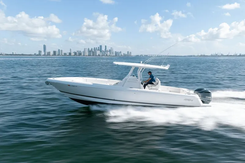 Slide: The Image of 2015 Intrepid 327 CC INFUSED boat cruising on open water with city skyline backdrop. - 6