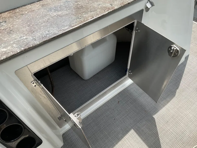 Slide: The Image of Open storage compartment on a 2019 Sylvan SE-CRS25 boat with a white container inside. - 13