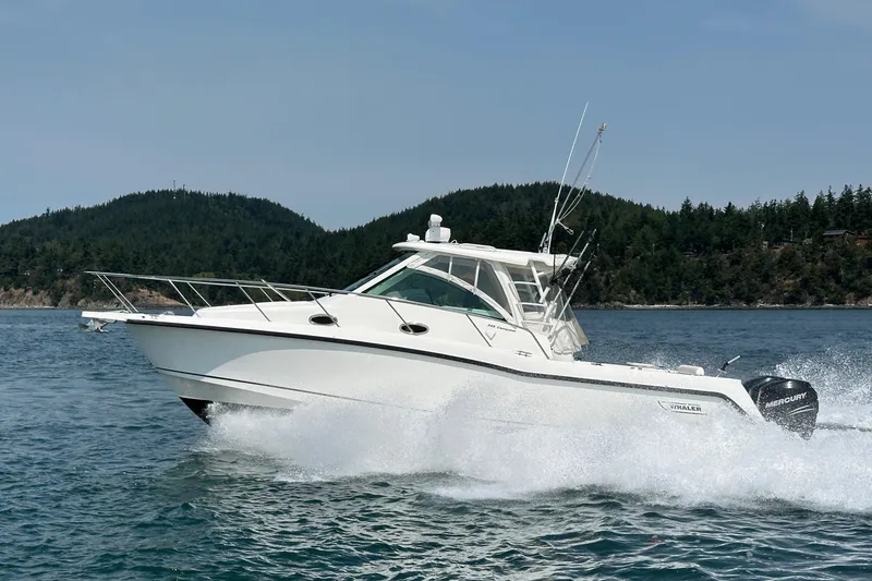Slide: The Image of 2013 Boston Whaler 345 Conquest cruising on water with scenic forested background. - 6