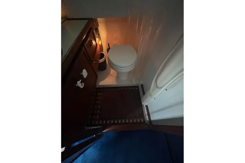 Slide: The Image of 1976 Uniflite 32 Sport Sedan bathroom with toilet, wooden cabinet, and shower area. - 50