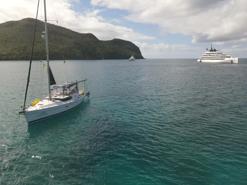 Slide: The Image of Sailboat "Hunter 45 Center Cockpit" anchored near lush island, with luxury yacht in background. - 17