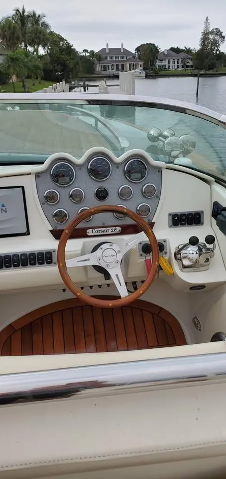 Slide: The Image of 2010 Chris-Craft Corsair 28 dashboard with wooden steering wheel and gauges, docked by a waterfront home. - 6