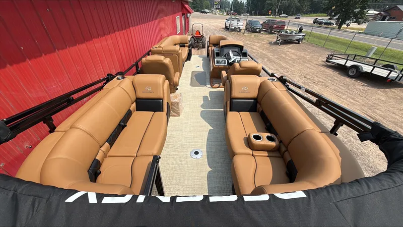 Slide: The Image of 2025 Regency 230 LE3 pontoon boat with tan seating, parked near a red building. - 4