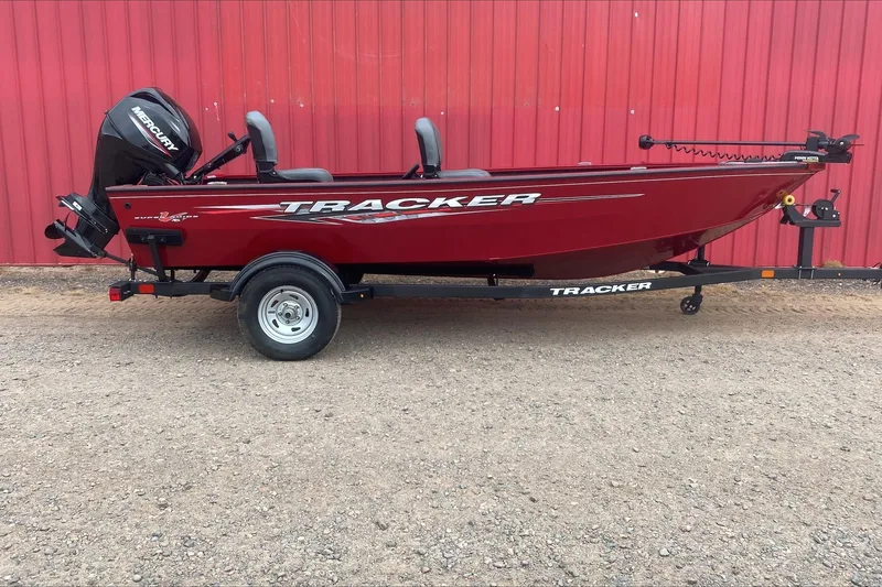 The Image of 2025 Tracker Super Guide V-16 T boat, red, on trailer, against red wall. - 0