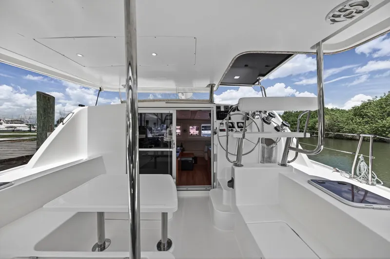 Slide: The Image of 2011 Leopard 38 catamaran cockpit with helm, seating, and table, docked by lush greenery. - 14
