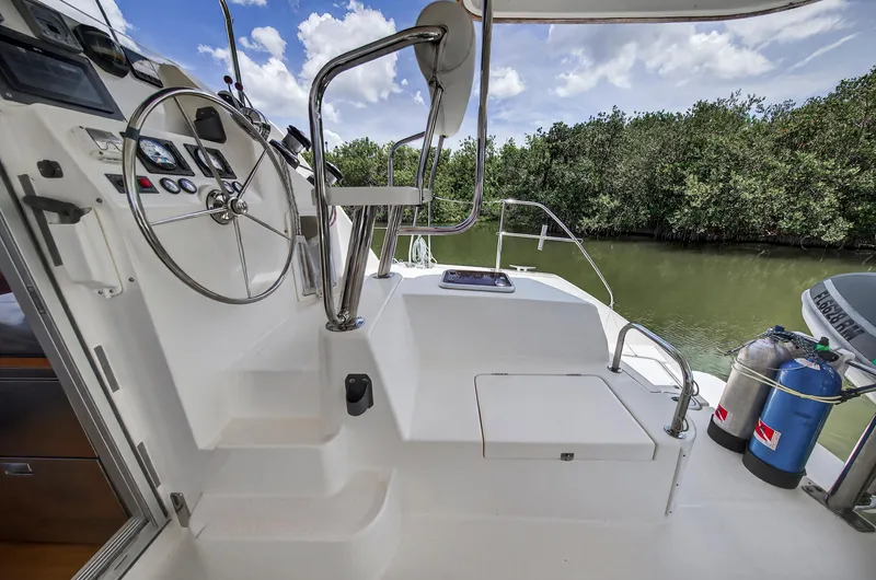 Slide: The Image of Helm of 2011 Leopard 38 catamaran with steering wheel and controls, docked near lush greenery. - 20