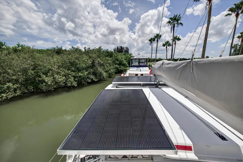 Slide: The Image of Leopard 38 catamaran with solar panels, docked near lush greenery and palm trees, under a cloudy sky. - 59