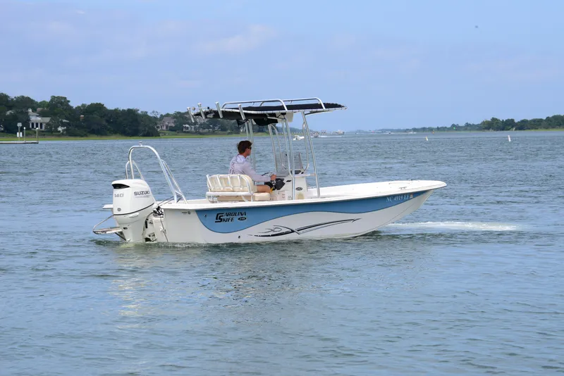 Slide: The Image of 2017 Carolina Skiff 218 DLV boat cruising on a calm lake with a Suzuki outboard motor. - 8