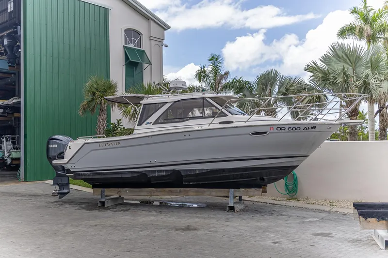 The Image of 2023 Cutwater C-248 Coupe boat on dry dock, surrounded by palm trees and a green building. - 0