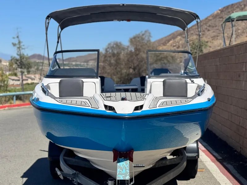 Slide: The Image of 2021 Yamaha Boats SX210 with blue hull, parked on a trailer, under a sunny sky. - 2