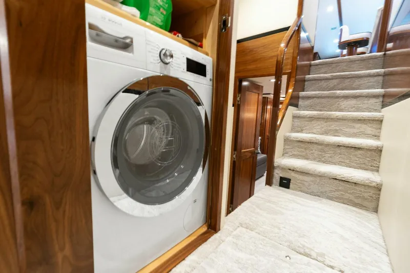 Slide: The Image of Laundry area inside 2023 Viking 80 Convertible yacht, featuring a modern washing machine and carpeted stairs. - 25