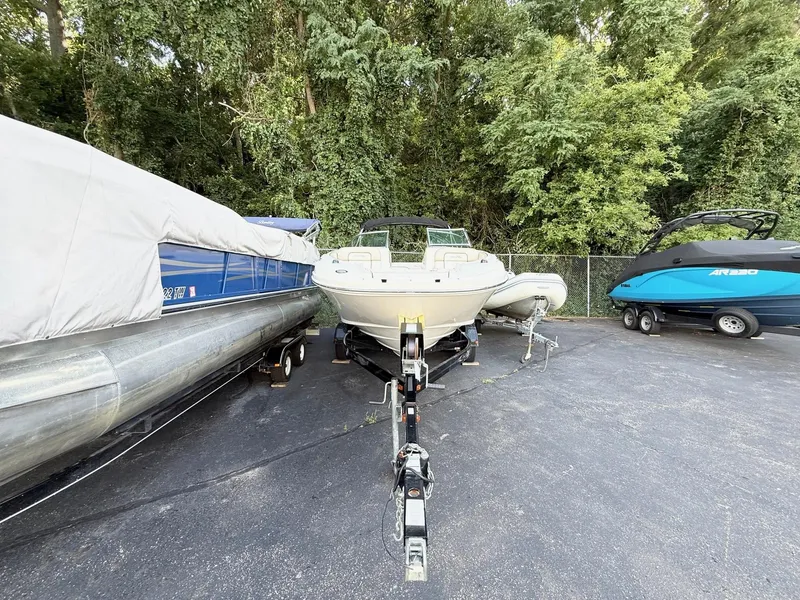 Slide: The Image of 2010 Sea Ray 220 Sundeck boat on trailer, parked between two other boats, surrounded by trees. - 3