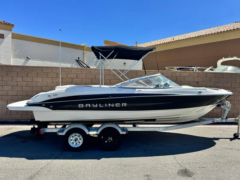 The Image of 2012 Bayliner 215 boat on trailer, parked outdoors under clear blue sky. - 0