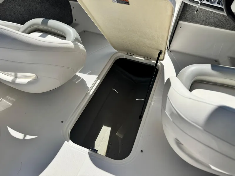 Slide: The Image of 2012 Bayliner 215 boat interior with open storage compartment between white seats. - 18