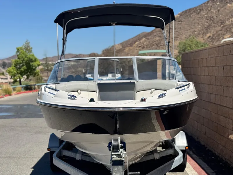 Slide: The Image of 2012 Bayliner 215 boat on trailer, parked outdoors with hills in background. - 2
