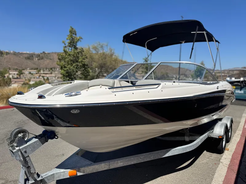 Slide: The Image of 2012 Bayliner 215 boat on trailer, parked outdoors under clear blue sky. - 3