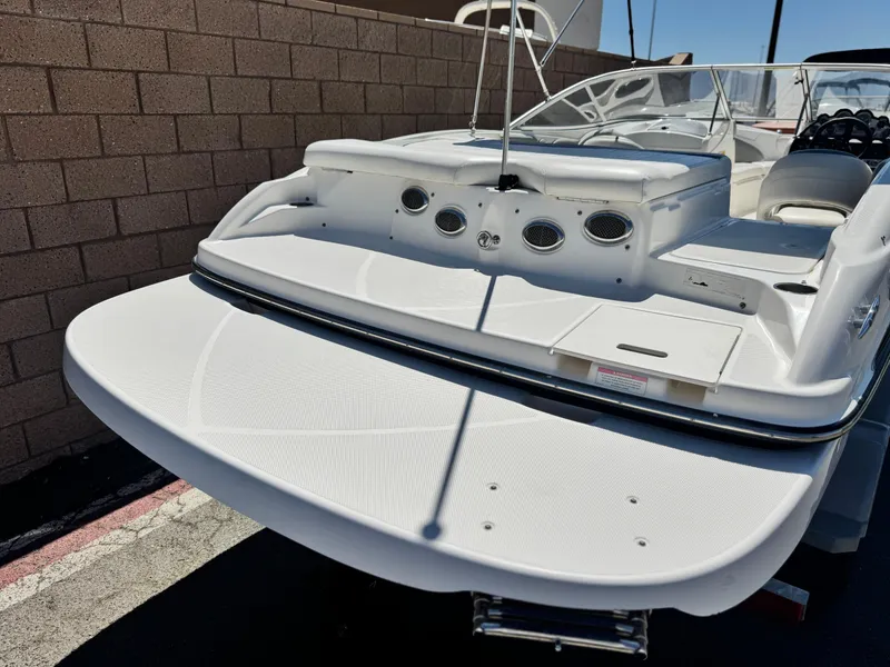 Slide: The Image of 2012 Bayliner 215 boat, rear view, white deck, parked near brick wall. - 6