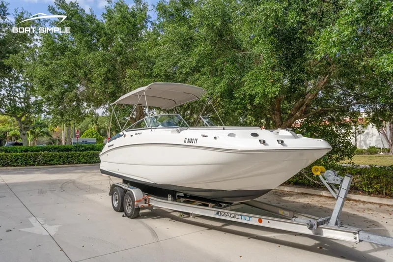 Slide: The Image of 2025 Hurricane SunDeck 2400 OB boat on trailer, parked outdoors with trees in background. - 3