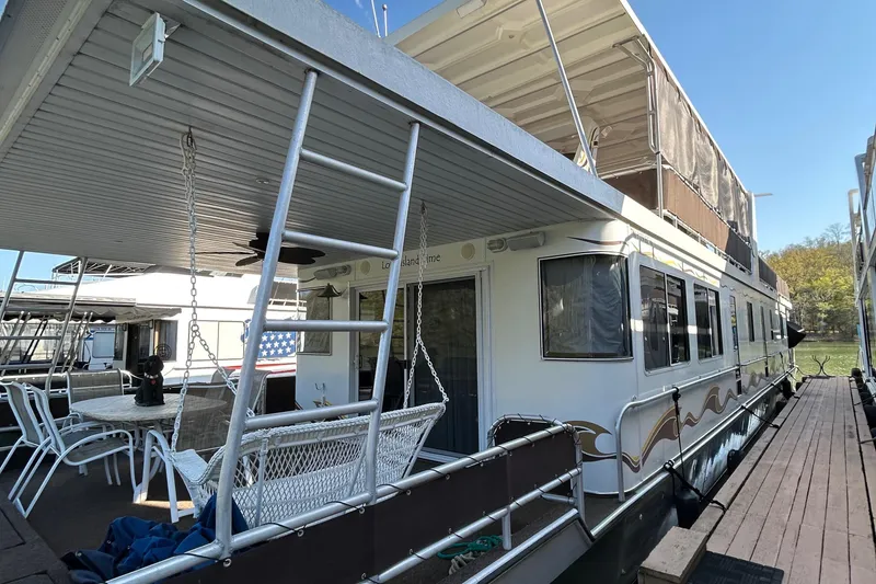 Slide: The Image of 2004 Horizon houseboat docked, featuring outdoor seating and ladder, under clear blue sky. - 1