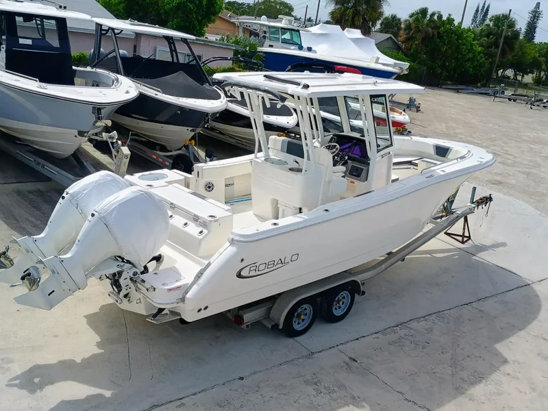 Slide: The Image of 2025 Robalo R270 Center Console boat on trailer, featuring dual engines, parked in a marina. - 3