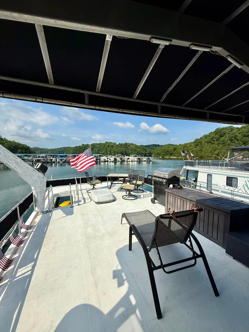 Slide: The Image of 1996 Jamestowner houseboat deck with seating, grill, and American flag on a scenic lake. - 19