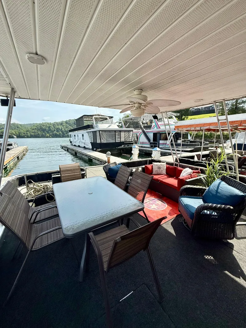 Slide: The Image of 1996 Jamestowner houseboat with outdoor seating, table, and ceiling fan, docked by a scenic lake. - 3