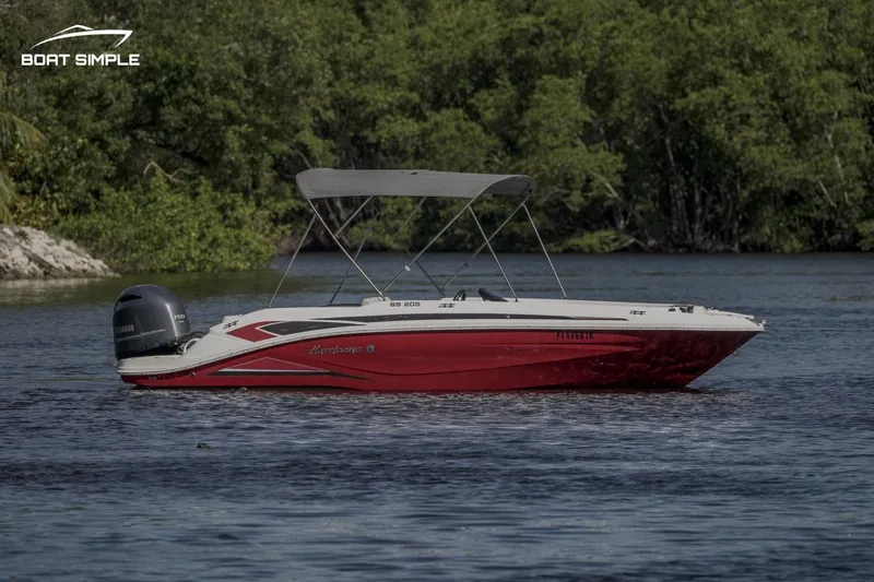 Slide: The Image of 2023 Hurricane SunDeck Sport 205 OB boat on calm water, surrounded by lush greenery. - 1