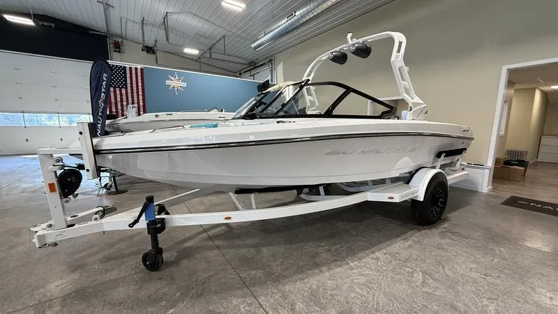 The Image of 2025 Nautique Ski 200 boat in showroom, white exterior, on trailer. - 1