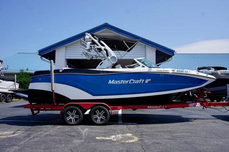 The Image of 2018 MasterCraft XT22 boat on red trailer, parked outside a building. - 1
