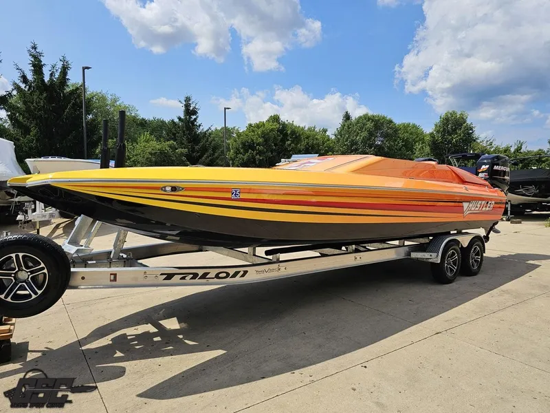 Slide: The Image of 2019 Hustler 25 Talon Cat speedboat on trailer, vibrant orange and yellow design, parked outdoors. - 25