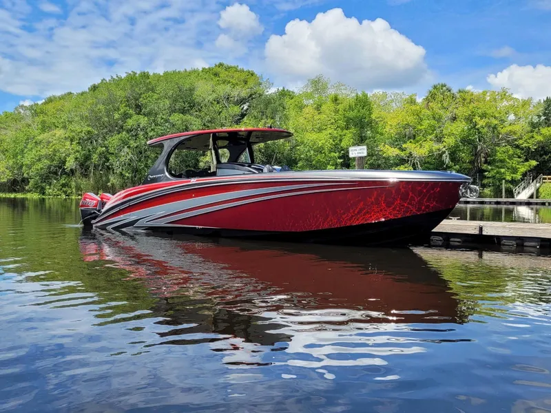 Slide: The Image of 2025 Mystic Powerboats M4200 in vibrant red, docked on a serene lake with lush greenery. - 2