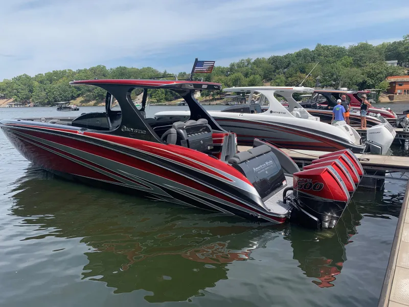 Slide: The Image of 2025 Mystic Powerboats M4200 in vibrant red, docked with powerful engines, surrounded by scenic water. - 3