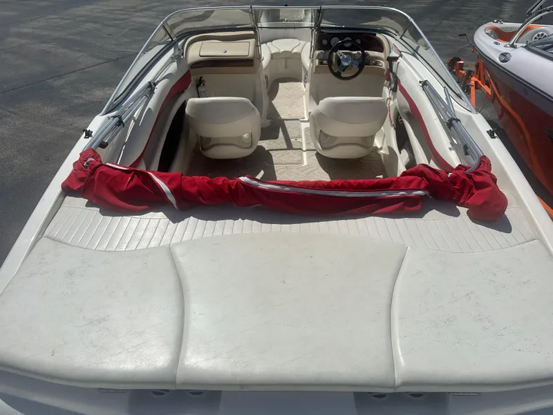Slide: The Image of 2008 Glastron 205 GX boat interior with white seating and red cover, parked on pavement. - 7