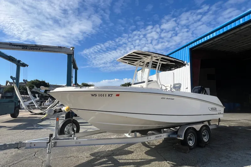 The Image of 2015 Boston Whaler 220 Outrage boat on trailer, parked outdoors under blue sky. - 0