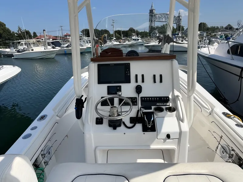 Slide: The Image of 2016 Regulator 23 boat dashboard with steering wheel and controls, docked in a marina. - 23
