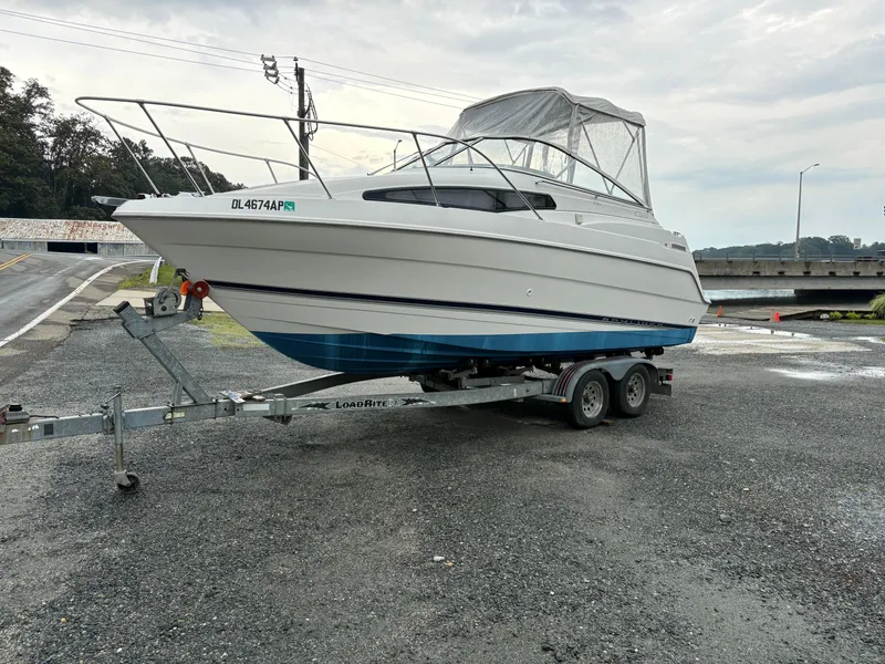 The Image of 1999 Bayliner 2355 SUNBRIDGE boat on trailer, parked near a road and waterway. - 1