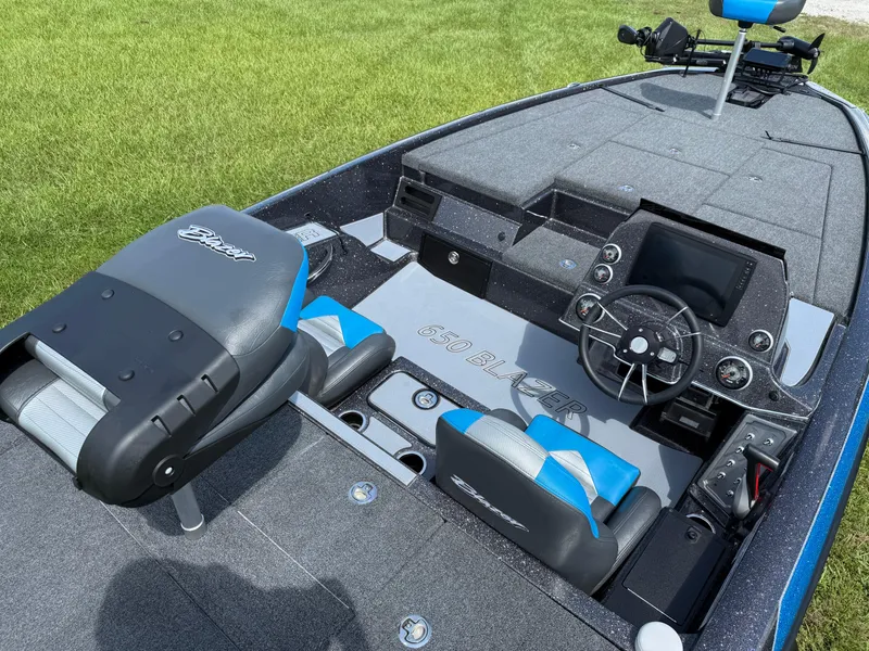 Slide: The Image of 2026 Blazer 650 NAP boat interior with steering console and seating on grassy background. - 12