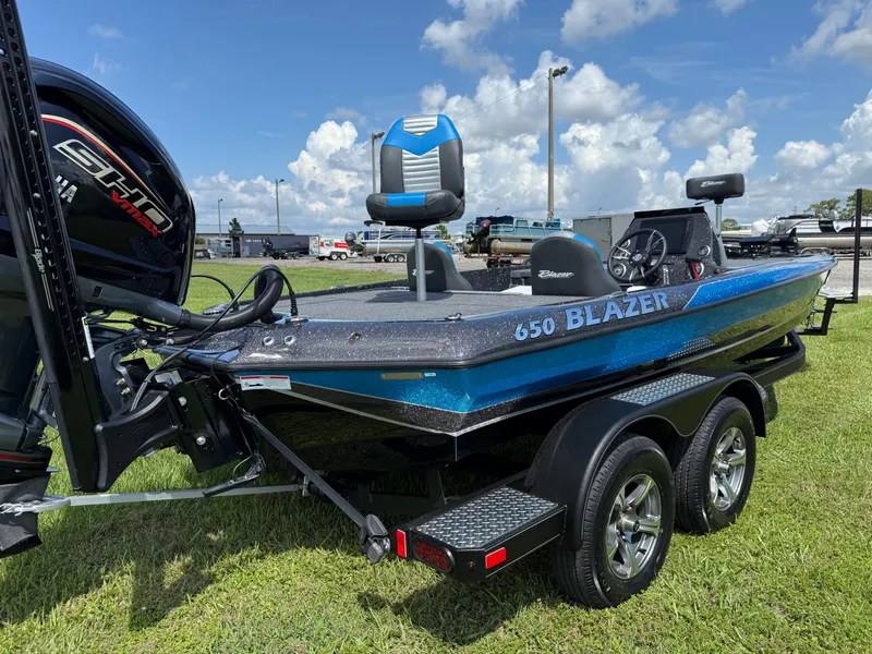 Slide: The Image of 2026 Blazer 650 NAP boat on trailer, blue and black design, parked on grass. - 17