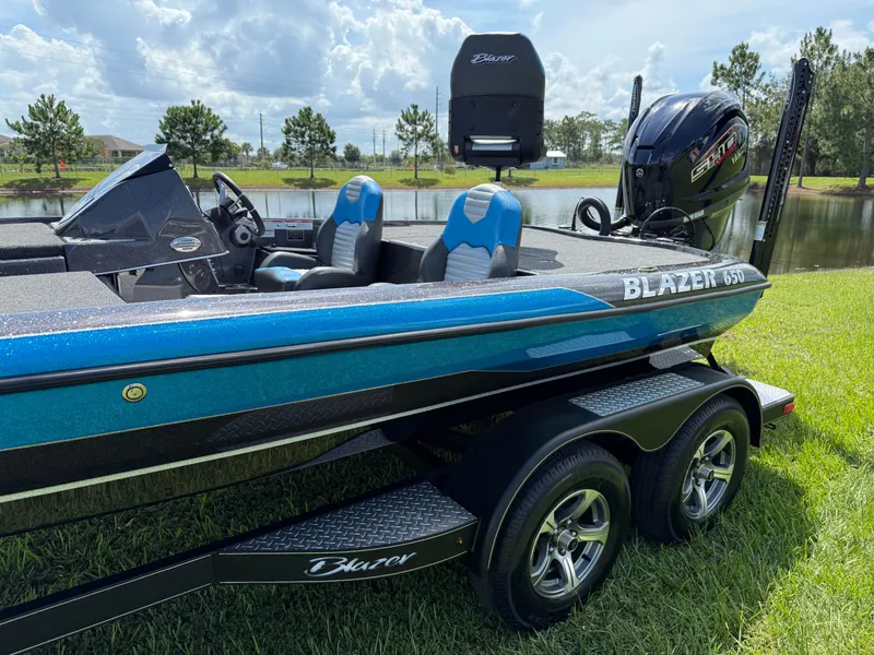Slide: The Image of 2026 Blazer 650 NAP boat on trailer by a lake, featuring blue and black design. - 5