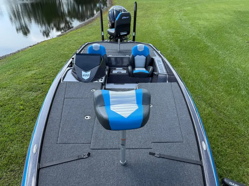 Slide: The Image of 2026 Blazer 650 NAP boat with blue and gray seating, near a serene lake. - 6